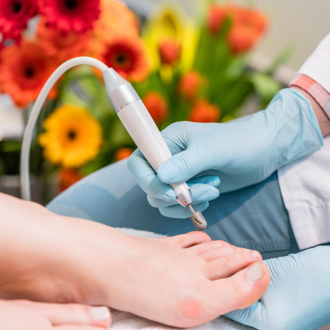 Close-up of the hands of a pedicurist wearing sterile surgical gloves while using a toe nail clipper, while shaping the nails of a female customer in a beauty salon